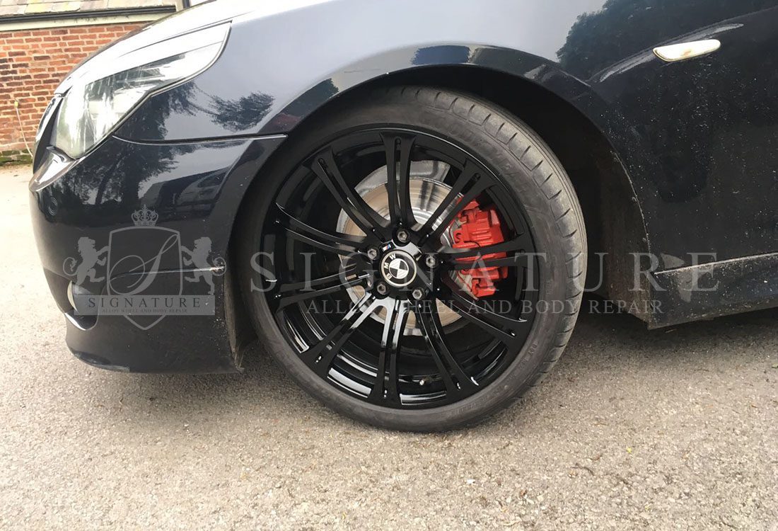 Refurbished gloss black BMW alloy wheel with a red brake caliper