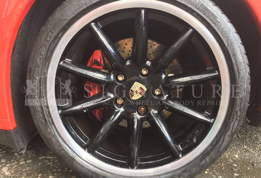 Black Porsche alloy wheel with a red brake caliper on a red car after refurbishment
