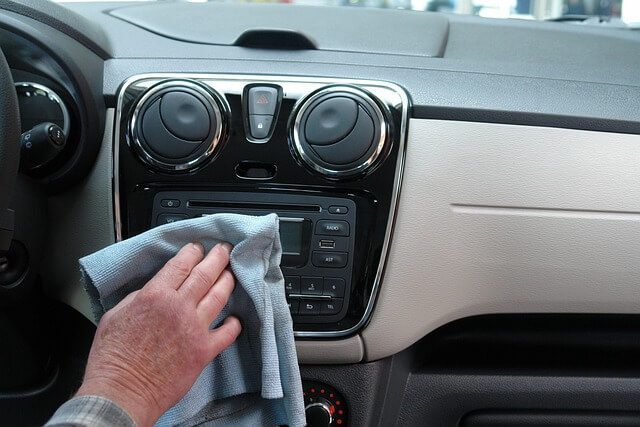 A hand wiping the dashboard and centre console of a car with a microfibre cloth