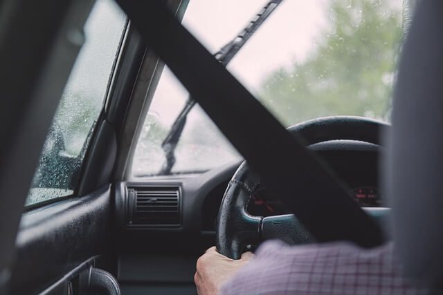 A driver holding the steering wheel, seen from the passenger seat on a wet day