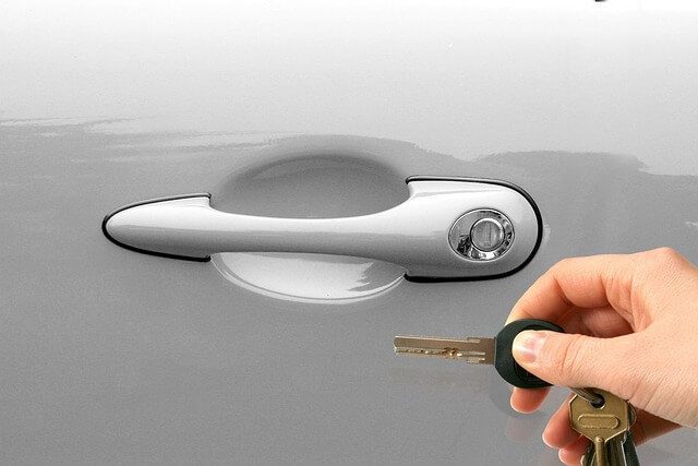 A hand holding a car key beside the door handle of a silver car