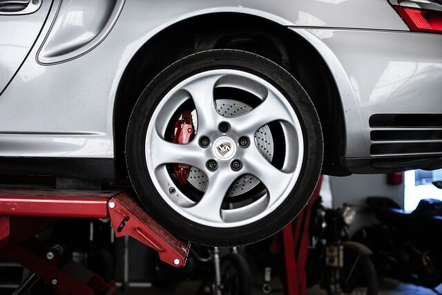 A silver sports car raised on a workshop ramp, showing the front alloy wheel and brake caliper