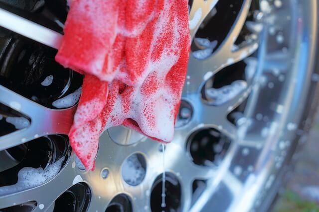 Person cleaning a car wheel with a brush and cleaning foam