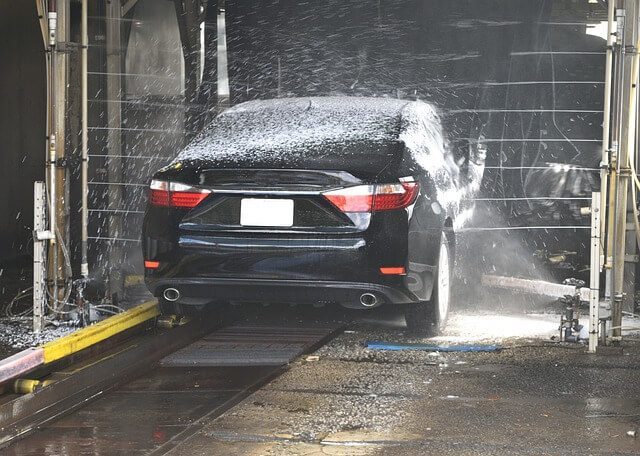 A dark saloon car covered in foam inside an automatic car wash