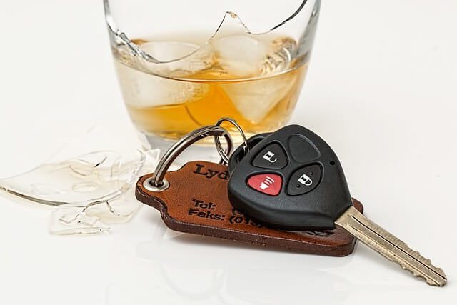 A glass of whisky with ice next to a car key on a leather fob and a piece of broken glass