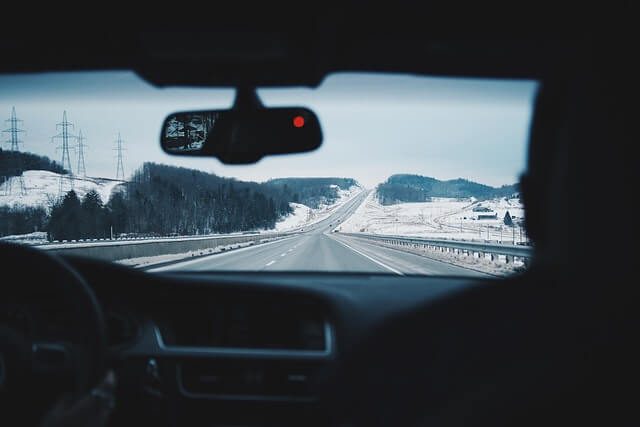 View through a car windscreen of a snow lined dual carriageway with the dashboard and rear view mirror in shot