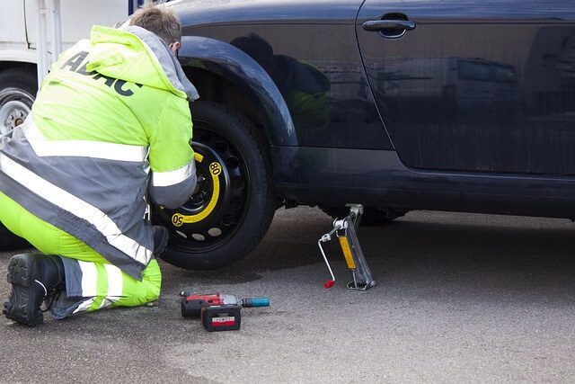 A technician in a high visibility jacket fitting a spare wheel to a car at the roadside