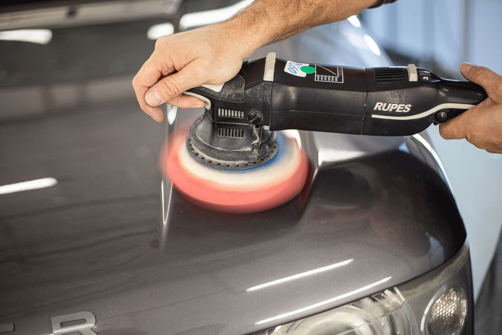A machine polisher being used on the panel of a car after washing